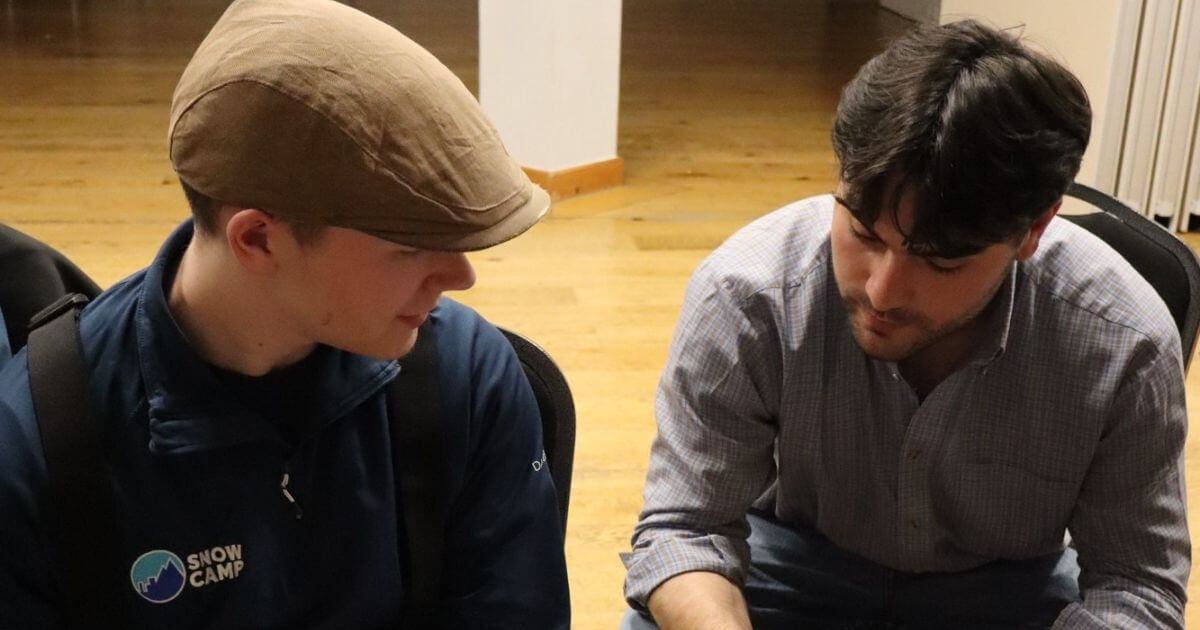 A young man in a Snow Camp jacket and cap listens closely to a mentor during a one-to-one coaching session, highlighting the personal guidance and career support offered through the Futures snow camp.
